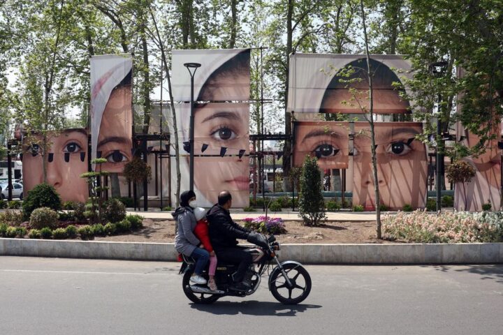 Ciudadanos iraníes pasan en coche junto a grandes retratos de las alumnas de la escuela Minab que murieron en un ataque aéreo en la plaza Tajrish de Teherán, el 21 de abril de 2026.