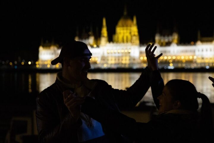 Varios jóvenes bailan encaramados a la orilla del Danubio frente al Parlamento